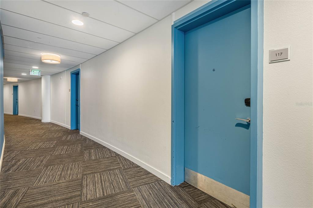 A hallway features blue doors, patterned carpet, and recessed lighting leading toward an exit sign — 225 CELEBRATION PLACE UNIT 117, CELEBRATION, FL