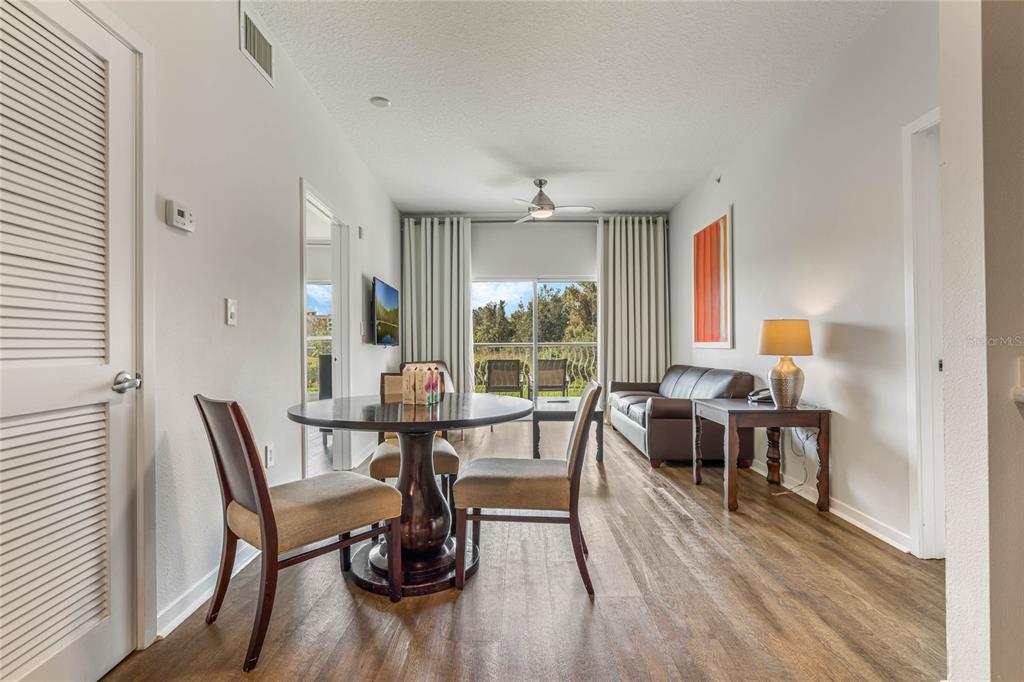 A dining area and living space feature wood-look flooring, a ceiling fan, and balcony access — 225 CELEBRATION PLACE UNIT 117, CELEBRATION, FL