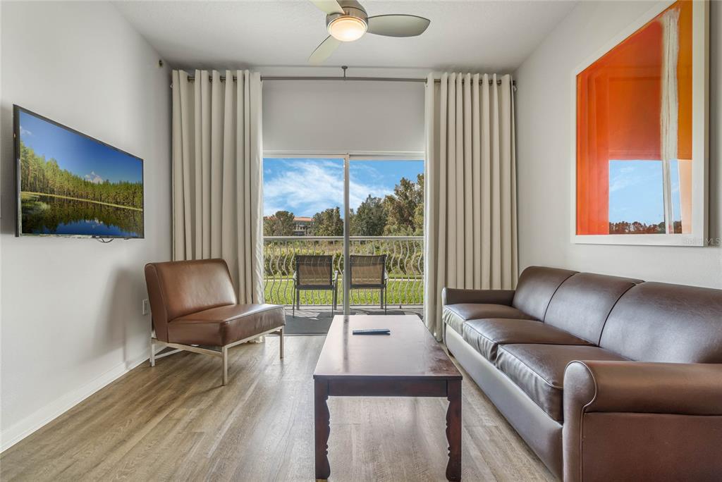 A living room features a brown leather sofa, an accent chair, and a sliding glass door — 225 CELEBRATION PLACE UNIT 117, CELEBRATION, FL