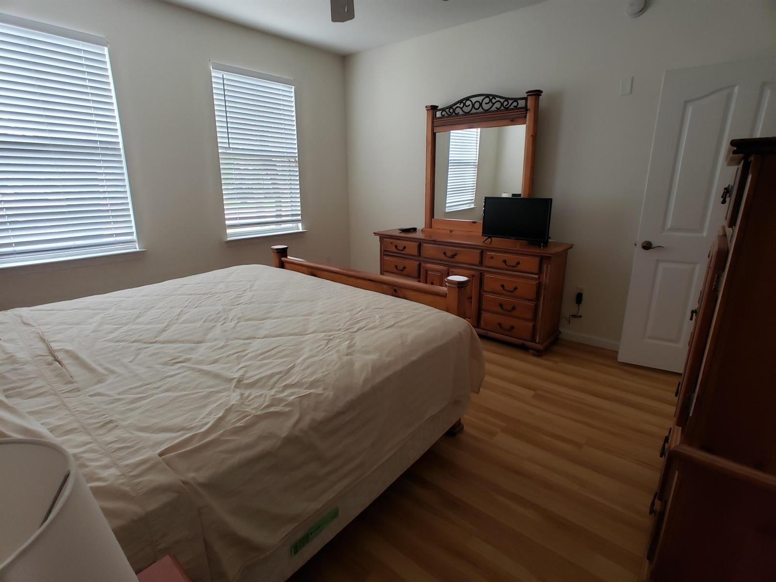 A bedroom features a wooden bed frame, a matching dresser with a mirror, and light flooring — 276 Murcia Drive # 111, Jupiter FL 33458, JUPITER, FL