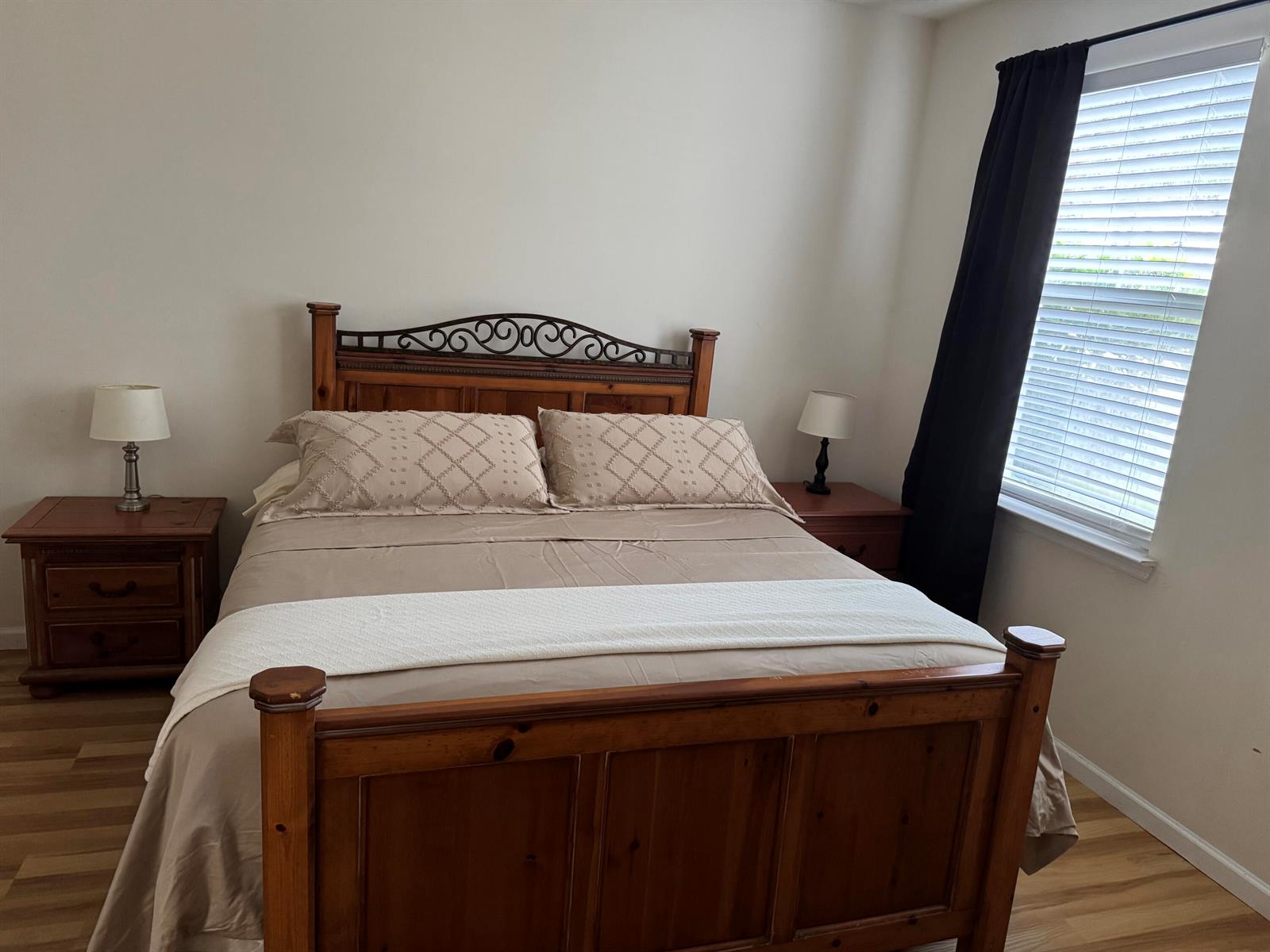 A bedroom features a wooden bed frame, two nightstands with lamps, and a window with curtains — 276 Murcia Drive # 111, Jupiter FL 33458, JUPITER, FL