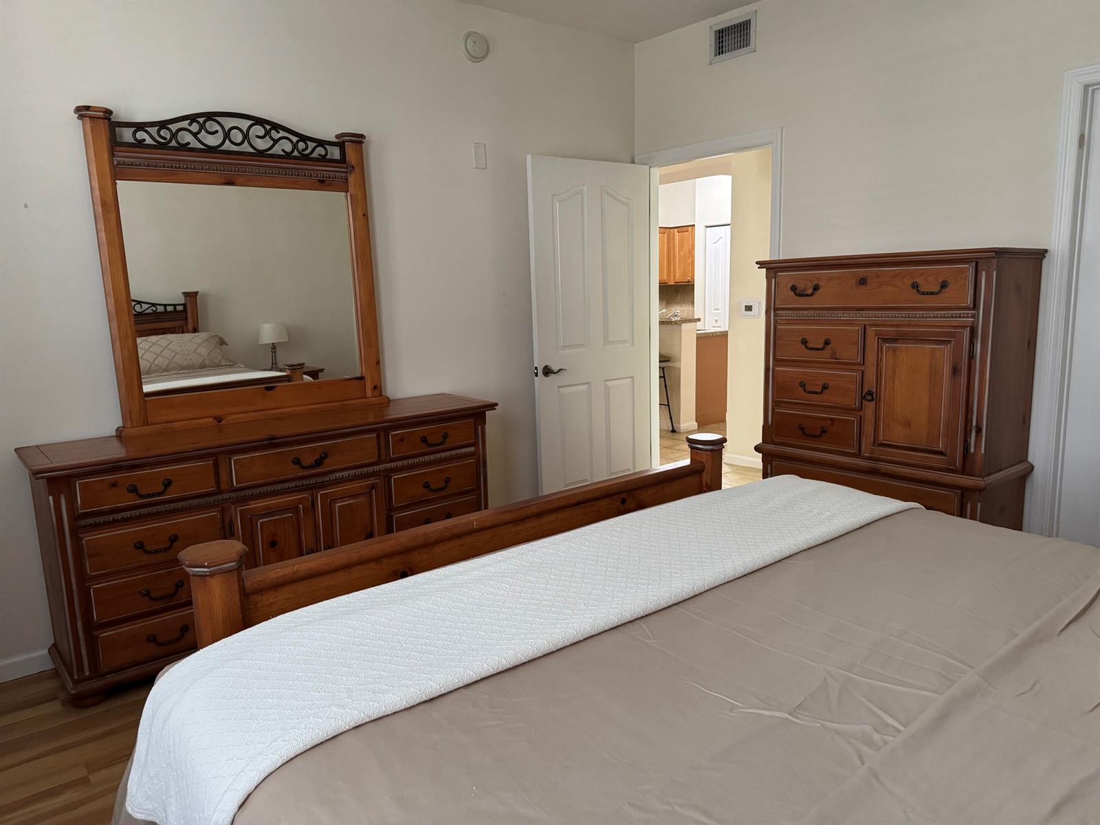 A bedroom with wood furniture, a large mirror, and a doorway leading to a kitchen — 276 Murcia Drive # 111, Jupiter FL 33458, JUPITER, FL