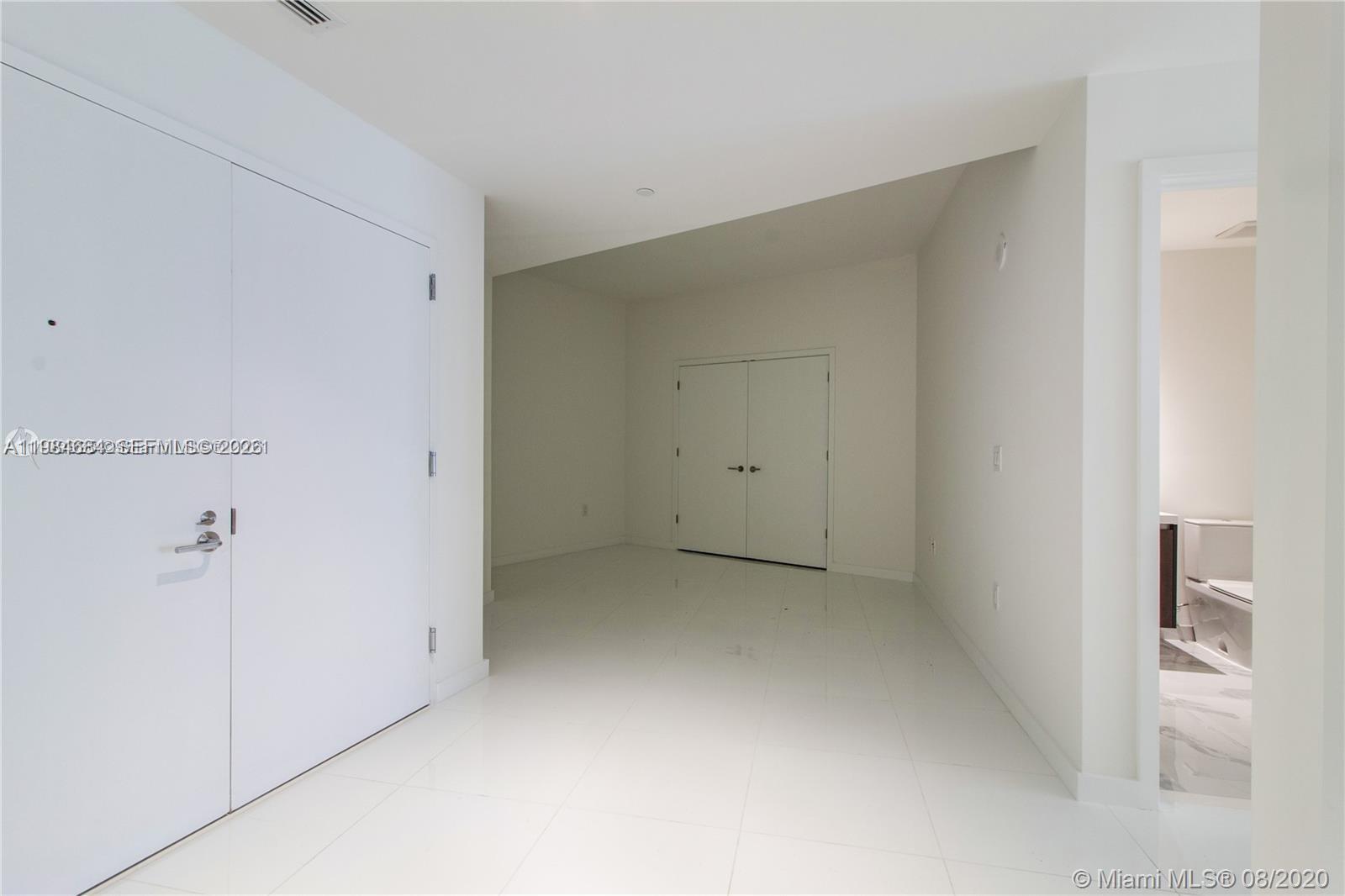 A white-walled room features glossy tile flooring, two sets of double doors, and a bathroom — 851 NE 1st Ave # 3601, Miami FL 33132, MIAMI, FL