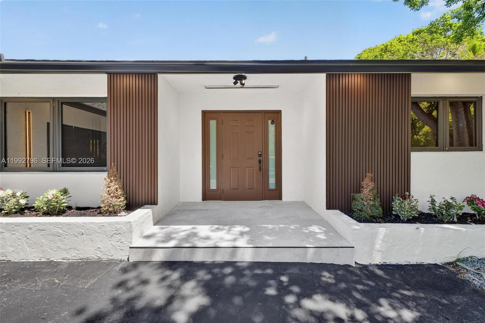 The exterior of a house features a brown front door, vertical wood paneling, and planters — 14755 SW 18th Ct, Davie FL 33325, DAVIE, FL