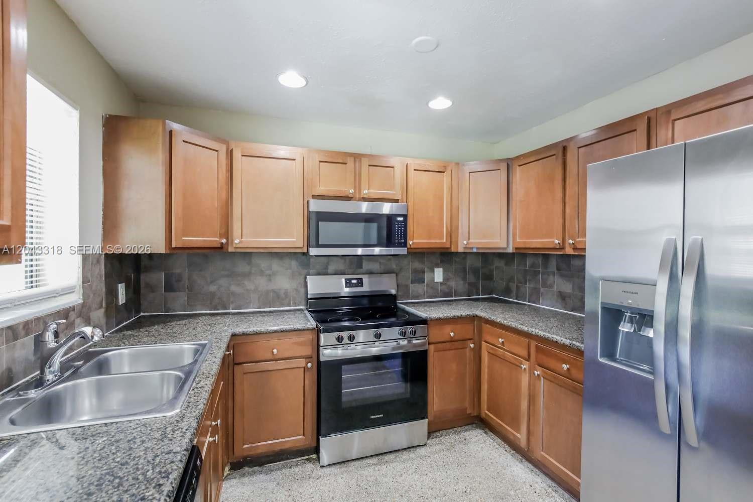 A kitchen features wood cabinets, granite countertops, stainless steel appliances, and a tiled backsplash — FORT LAUDERDALE, FL