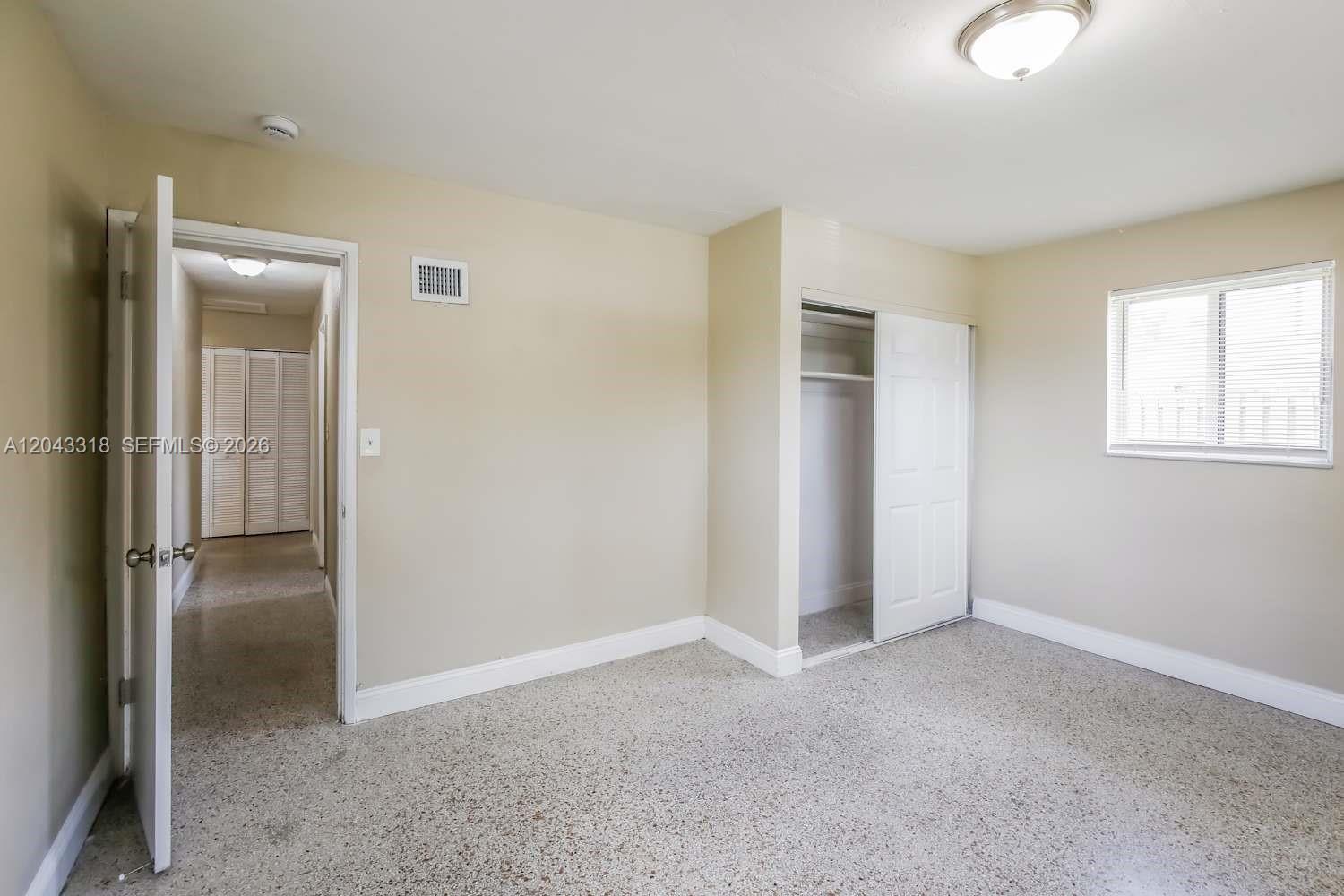 A bedroom features beige walls, carpeted flooring, a window with blinds, and a sliding closet — FORT LAUDERDALE, FL