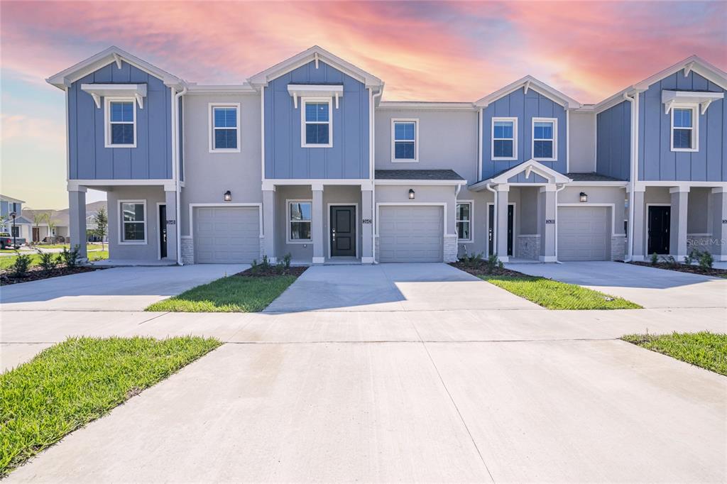A row of four modern townhomes with blue siding, gray garages, and concrete driveways — 2642 RUNNERS CIRCLE, CLERMONT, FL