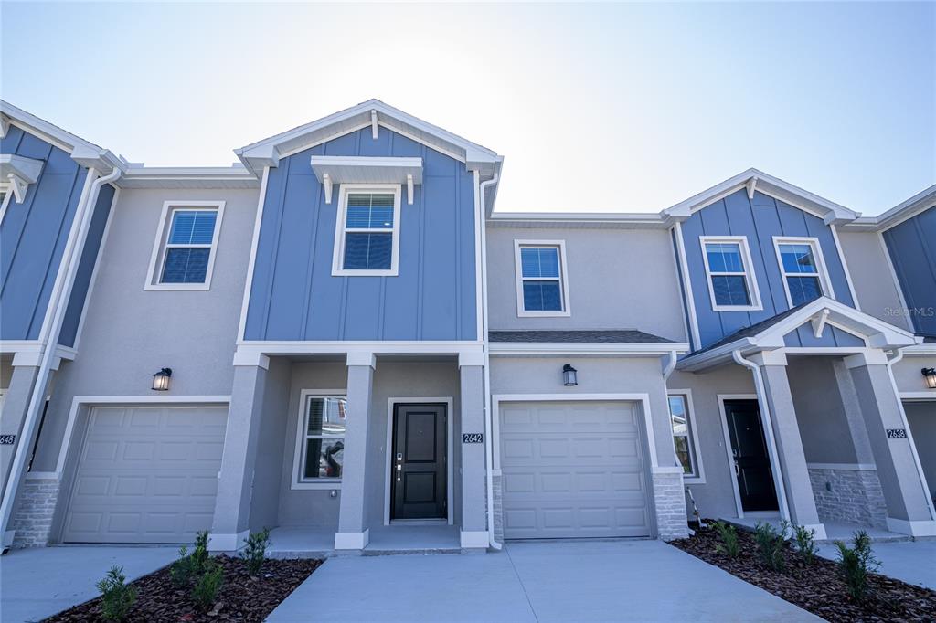 A row of modern townhomes features blue vertical siding, light gray stucco, and attached garages — 2642 RUNNERS CIRCLE, CLERMONT, FL