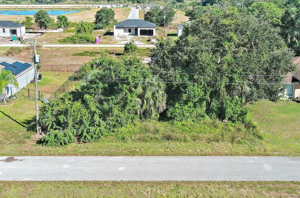 An aerial view shows a vacant, tree-covered residential lot situated between two houses — 341 Ranchito Ave, Lehigh Acres FL 33974, LEHIGH ACRES, FL