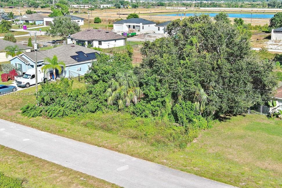 An aerial view shows a vacant, tree-covered lot situated between suburban residential houses — 341 Ranchito Ave, Lehigh Acres FL 33974, LEHIGH ACRES, FL