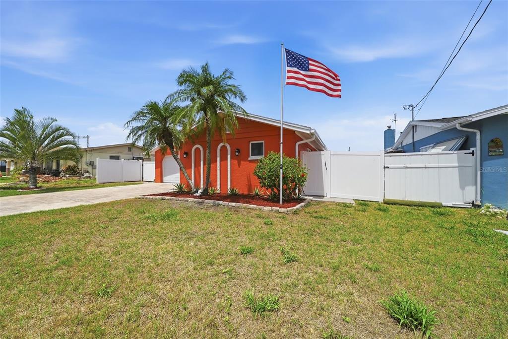 An orange house with a white fence and an American flag in the front yard — 13815 PLUMOSA AVENUE, HUDSON, FL