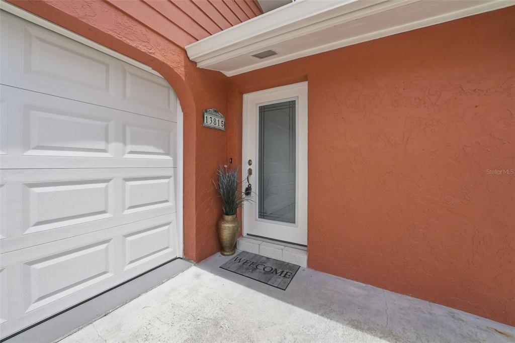A white front door with a glass panel sits next to a white garage door — 13815 PLUMOSA AVENUE, HUDSON, FL