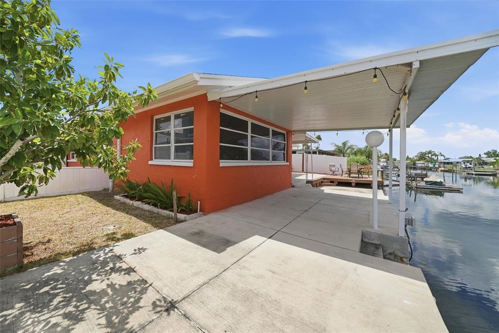 An orange house exterior features a concrete patio, a covered carport, and a waterfront view — 13815 PLUMOSA AVENUE, HUDSON, FL