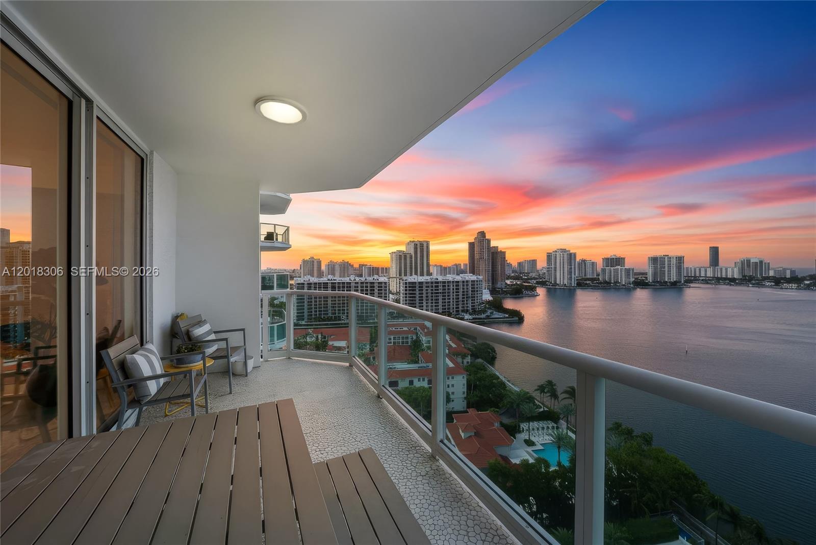 A balcony with outdoor furniture overlooks a bay and city skyline at sunset — 3301 NE 183rd St # 2007, Aventura FL 33160, AVENTURA, FL