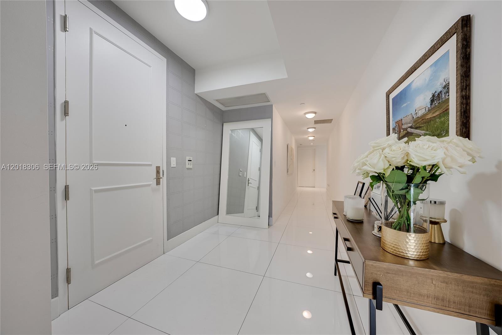 A bright hallway features white tile floors, a console table with flowers, and a mirror — 3301 NE 183rd St # 2007, Aventura FL 33160, AVENTURA, FL