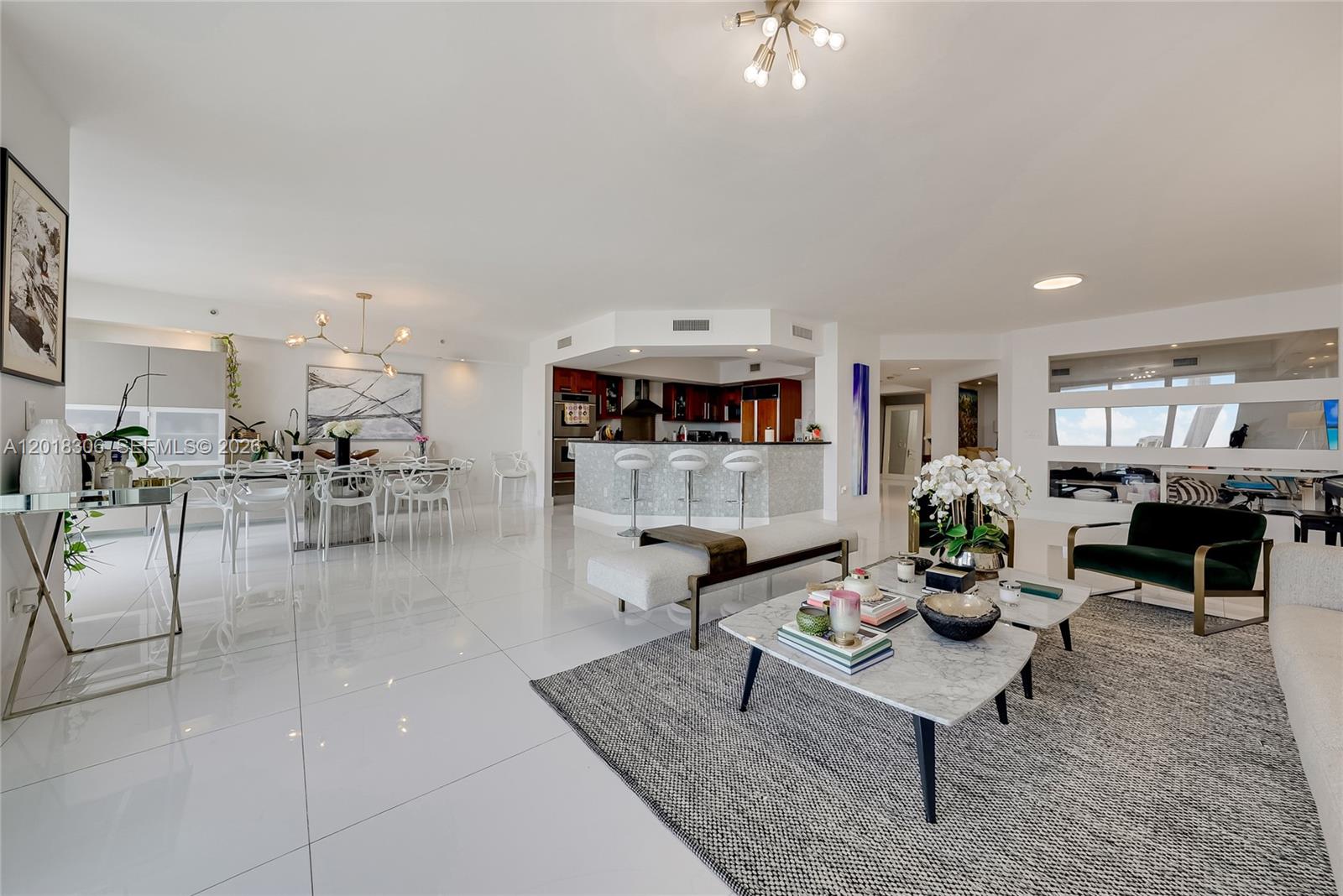 An open-concept living and dining area features white tile floors, a kitchen island, and modern furniture — 3301 NE 183rd St # 2007, Aventura FL 33160, AVENTURA, FL