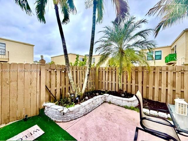 A fenced backyard patio features a raised stone planter, palm trees, and outdoor furniture — 1569 Shaker Cir, Wellington FL 33414, WELLINGTON, FL