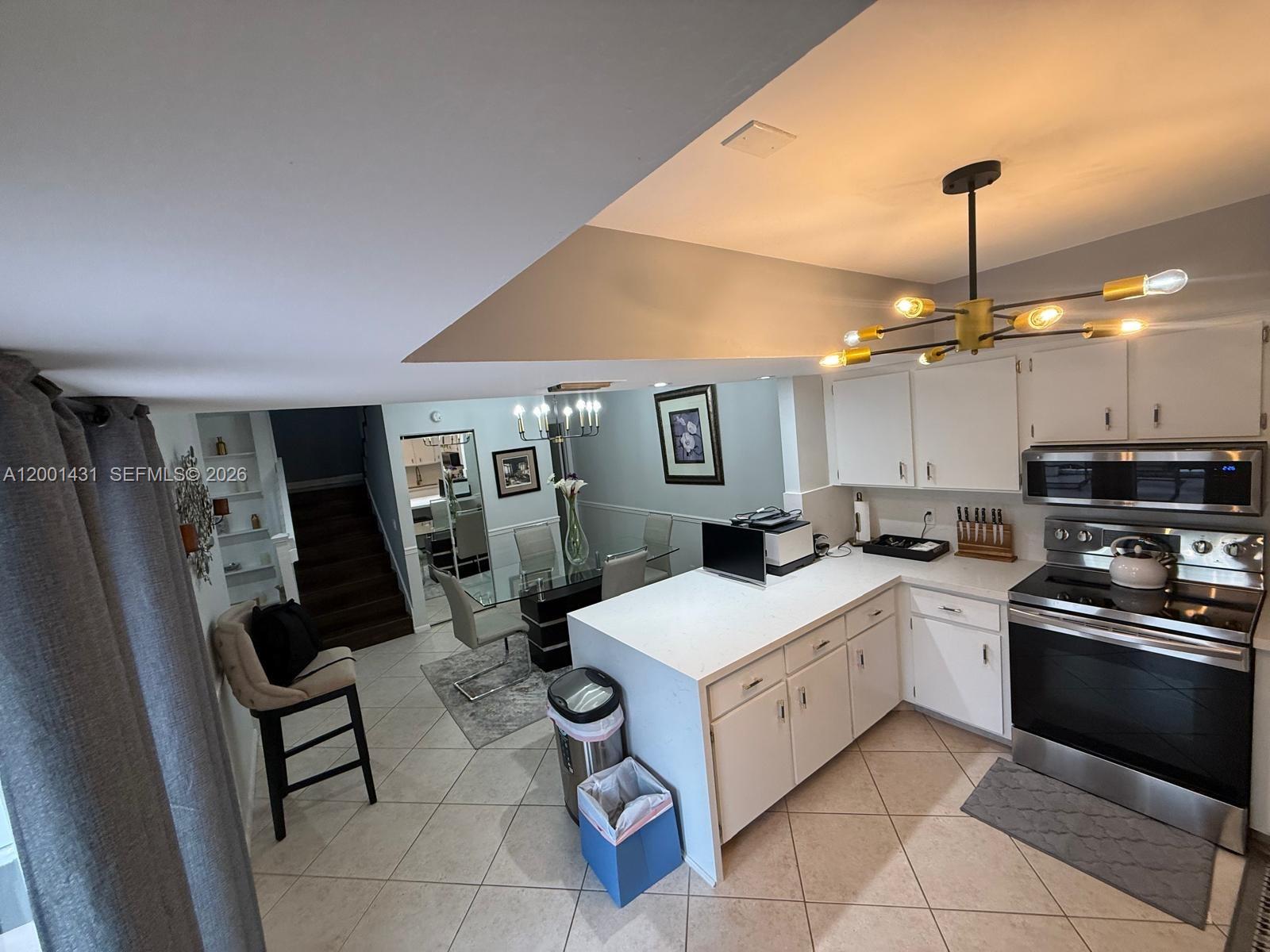 A kitchen with white cabinets and countertops opens into a dining area with stairs — 1569 Shaker Cir, Wellington FL 33414, WELLINGTON, FL