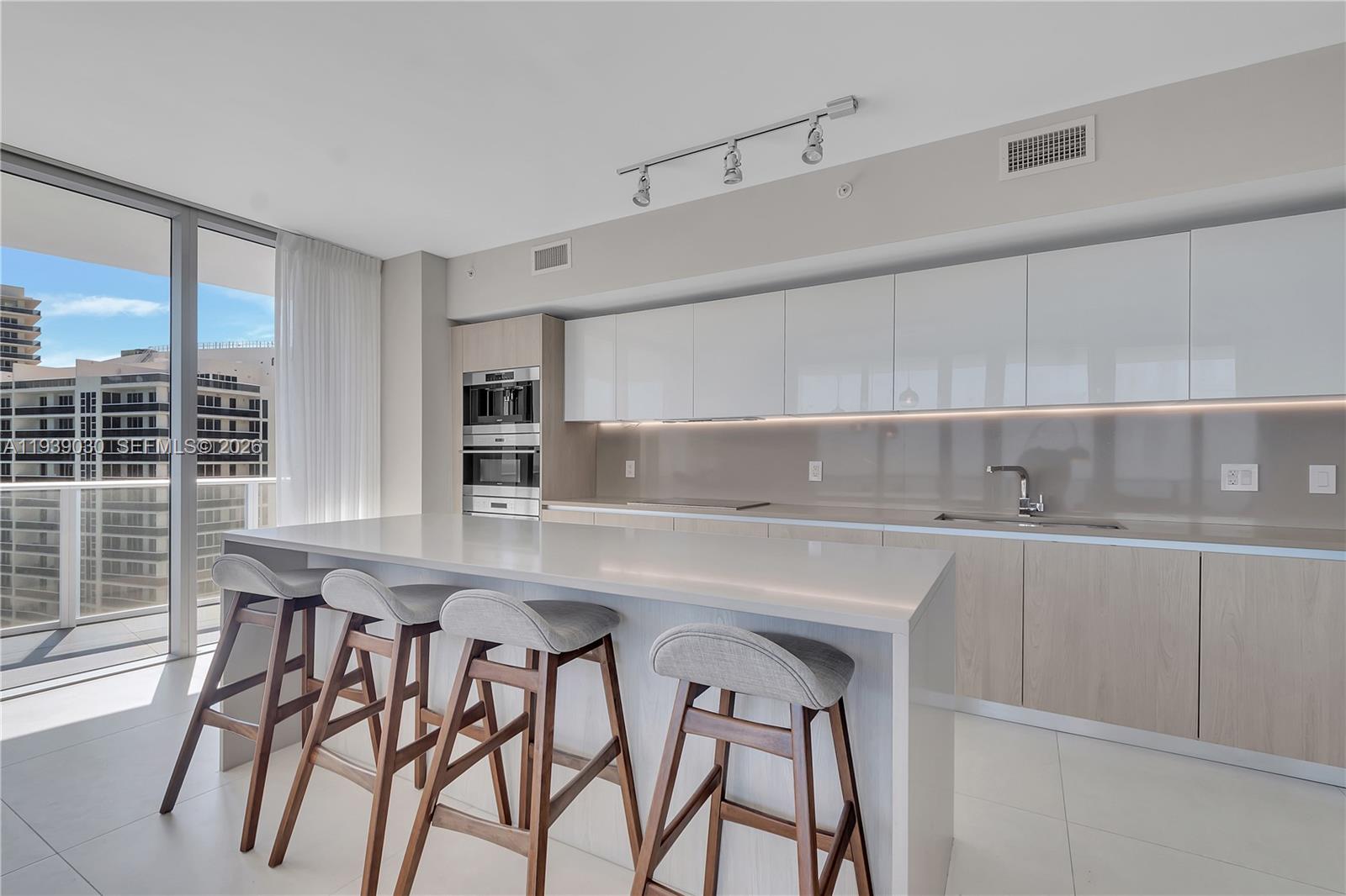A modern kitchen features a white island with four stools, light wood cabinetry, and balcony views — 4111 S Ocean Dr # 3601, Hollywood FL 33019, HOLLYWOOD, FL