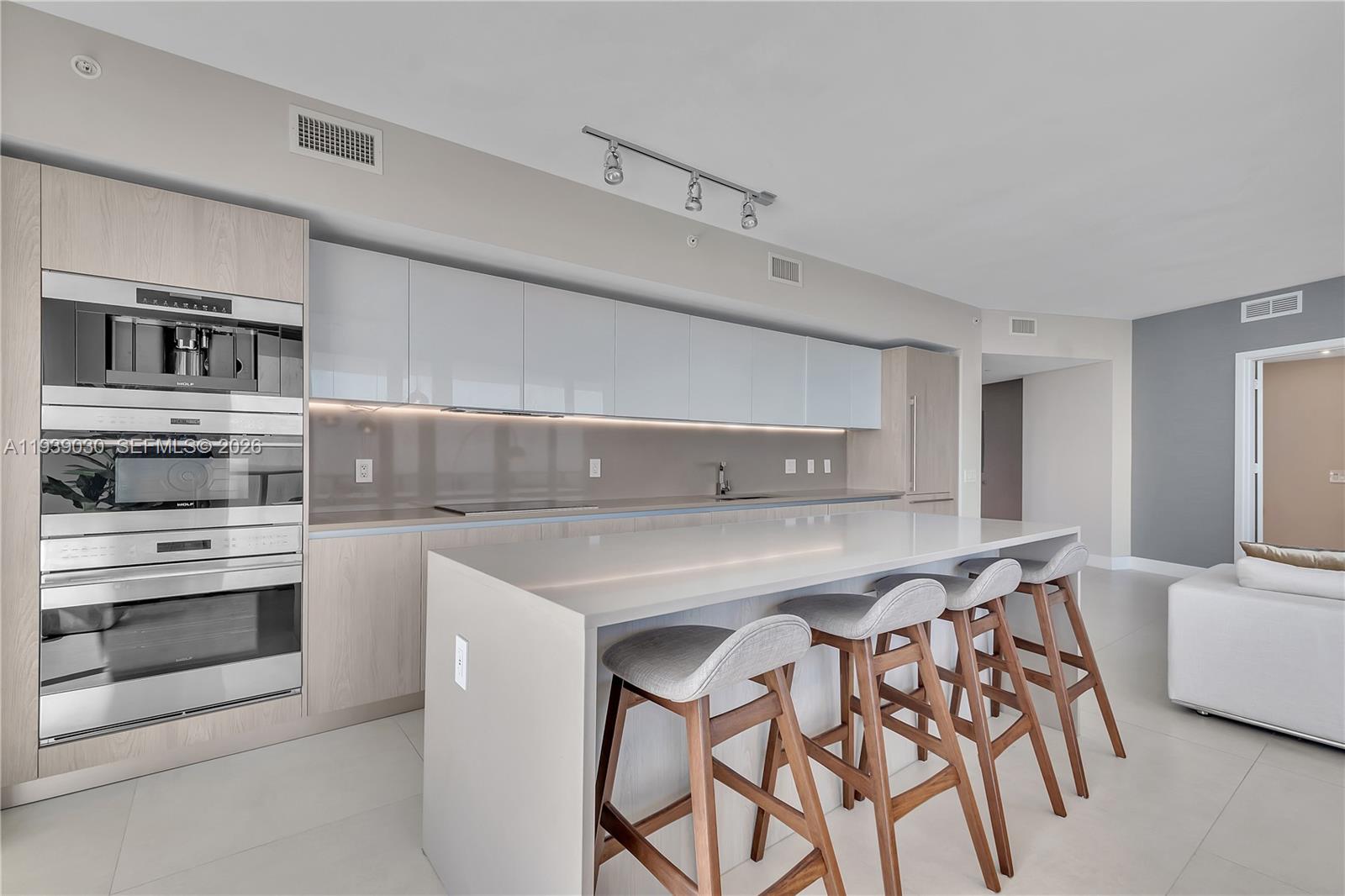 A modern kitchen features light wood cabinetry, white countertops, an island with stools, and appliances — 4111 S Ocean Dr # 3601, Hollywood FL 33019, HOLLYWOOD, FL