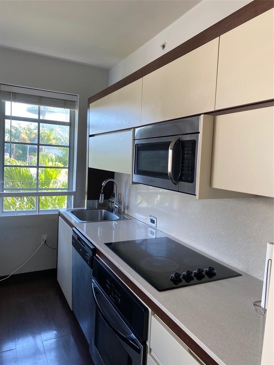 A modern kitchen features light-colored cabinetry, stainless steel appliances, and a window overlooking palm trees — 435 21st St # 307, Miami Beach FL 33139, MIAMI BEACH, FL