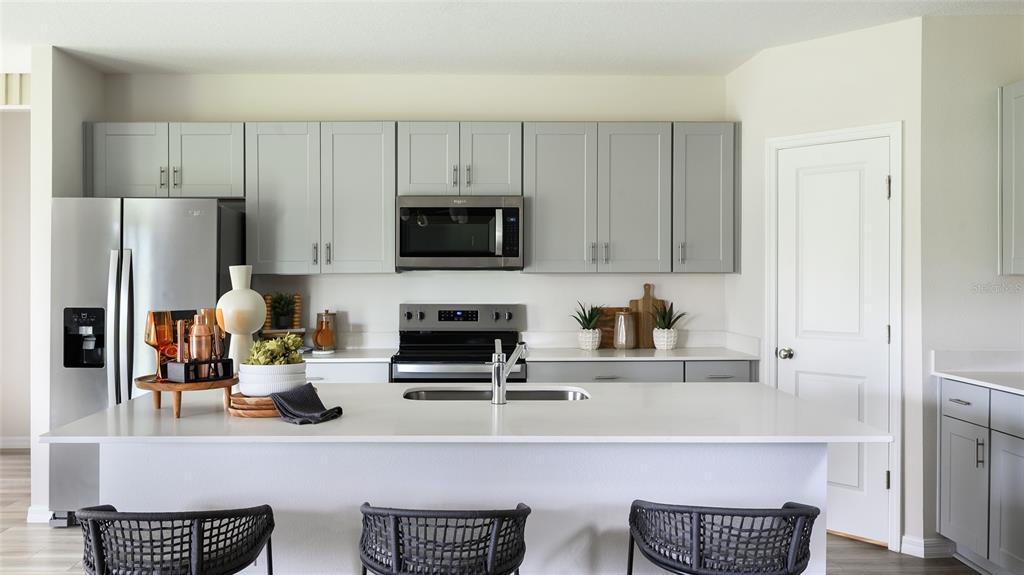 A modern kitchen features gray cabinets, a white island with bar stools, and stainless appliances — 31699 BARONNE STREET, WESLEY CHAPEL, FL