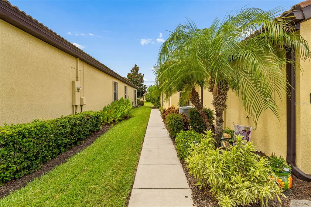 A narrow concrete walkway runs between two yellow stucco buildings with landscaped hedges and palms — 322 MYSTIC FALLS DRIVE, APOLLO BEACH, FL