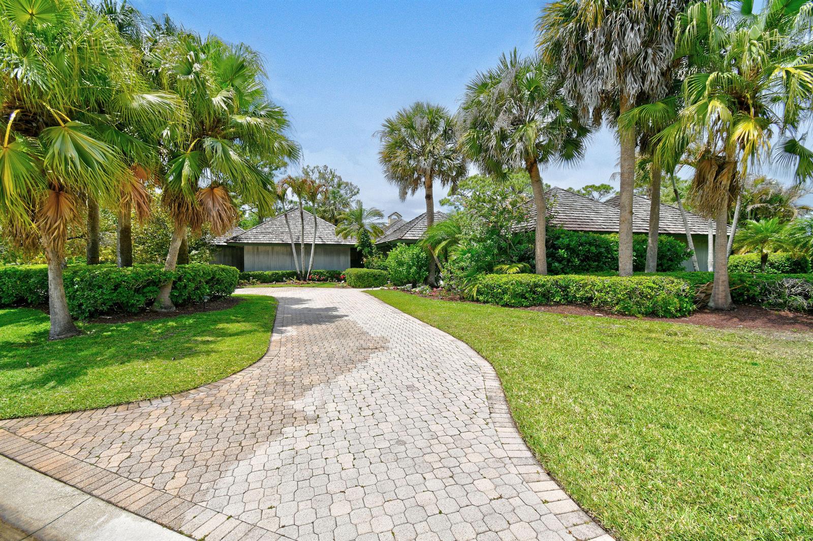 A paved driveway leads to a house surrounded by palm trees and manicured landscaping — 6980 SE Winged Foot Drive, Stuart FL 34997, STUART, FL