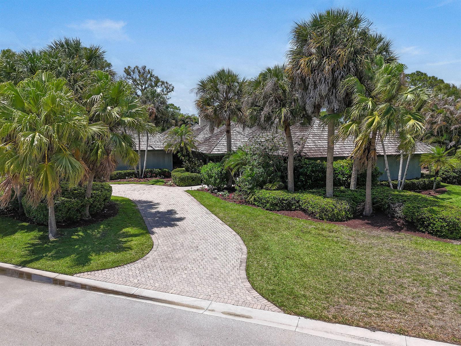 A paved driveway leads to a house with a shingled roof surrounded by palm trees — 6980 SE Winged Foot Drive, Stuart FL 34997, STUART, FL
