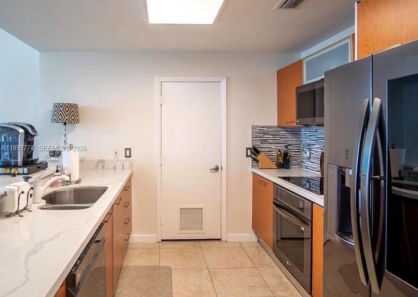 A galley-style kitchen features light countertops, wood cabinetry, stainless steel appliances, and tile flooring — 9066 SW 73rd Ct # 806, Miami FL 33156, MIAMI, FL