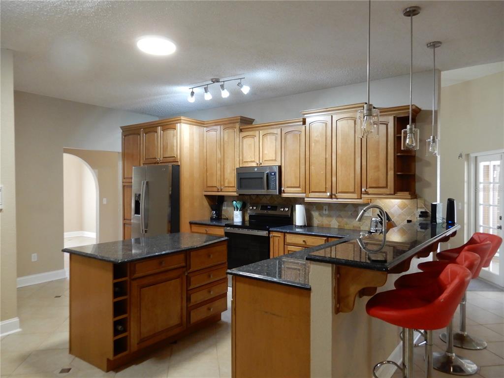 A kitchen features light wood cabinets, dark granite countertops, a center island, and red stools — 626 7TH AVENUE N, TIERRA VERDE, FL