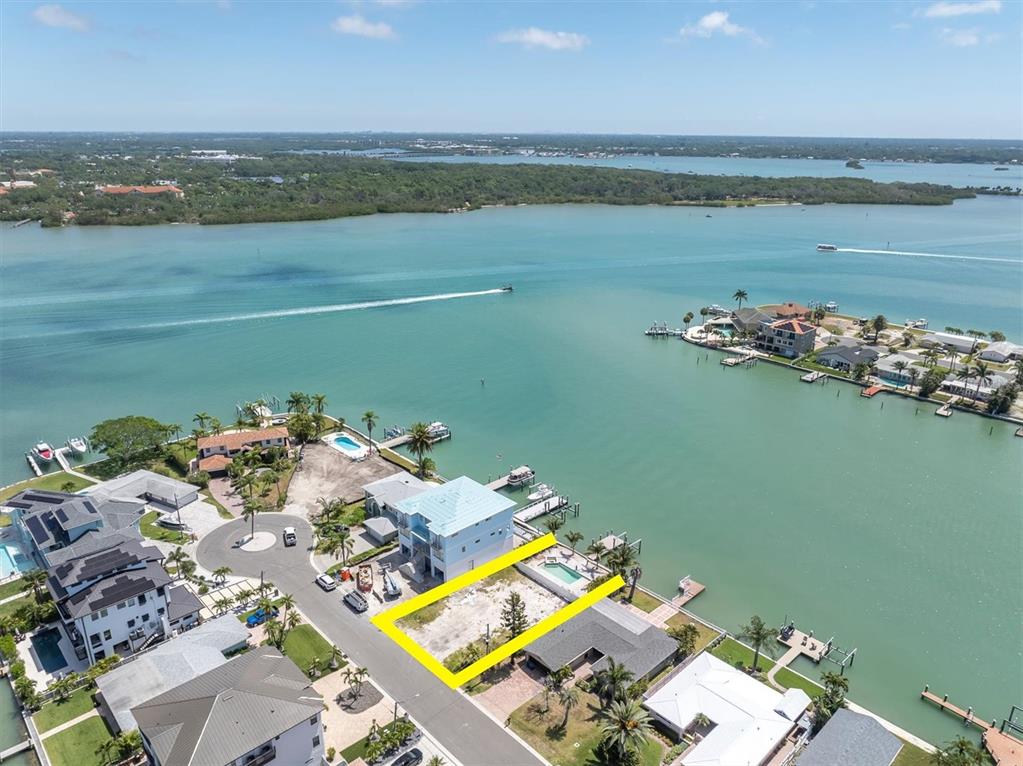 An aerial view shows a vacant waterfront lot outlined in yellow next to a house — 575 CRYSTAL DRIVE, MADEIRA BEACH, FL