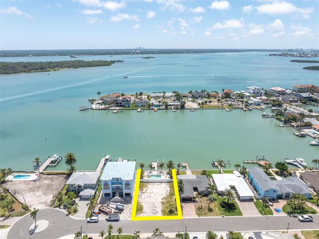 An aerial view shows a vacant waterfront lot highlighted in yellow between two houses — 575 CRYSTAL DRIVE, MADEIRA BEACH, FL