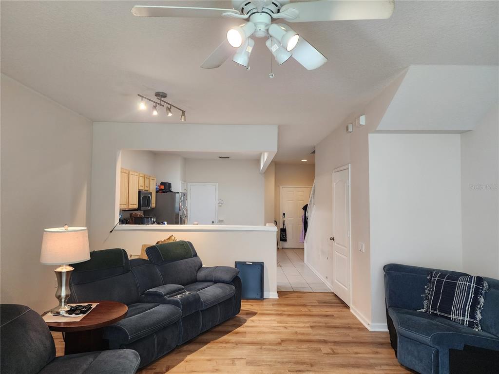 A living room with wood-look flooring, blue sofas, and a view into the kitchen area — 26541 CHIMNEY SPIRE LANE, WESLEY CHAPEL, FL