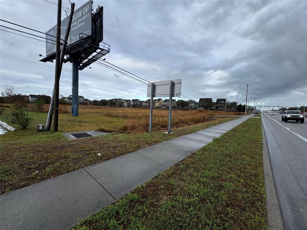 A vacant, grassy lot sits beside a sidewalk and a road with a large billboard — 11065 E COLONIAL DRIVE, ORLANDO, FL