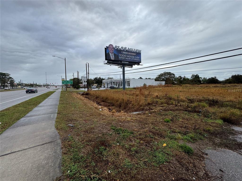 A vacant, grassy lot sits beside a sidewalk and a road with a large billboard — 11065 E COLONIAL DRIVE, ORLANDO, FL