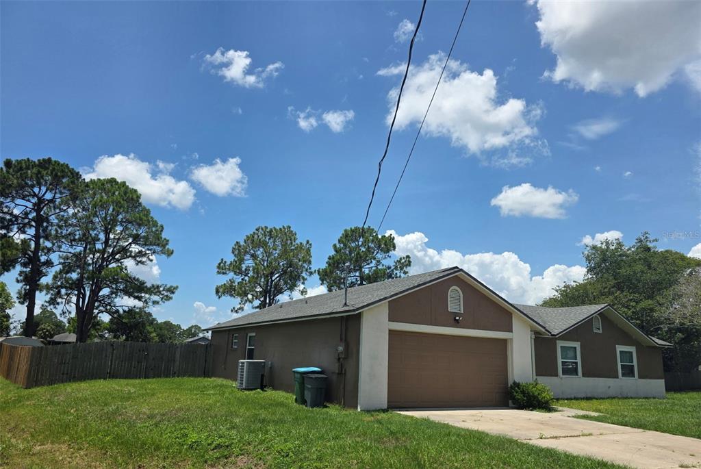 A brown single-story house with a two-car garage and a fenced yard under a blue sky — 2473 BECK CIRCLE, DELTONA, FL