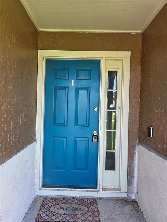 A blue front door with a side window and a welcome mat at the entrance — 2473 BECK CIRCLE, DELTONA, FL