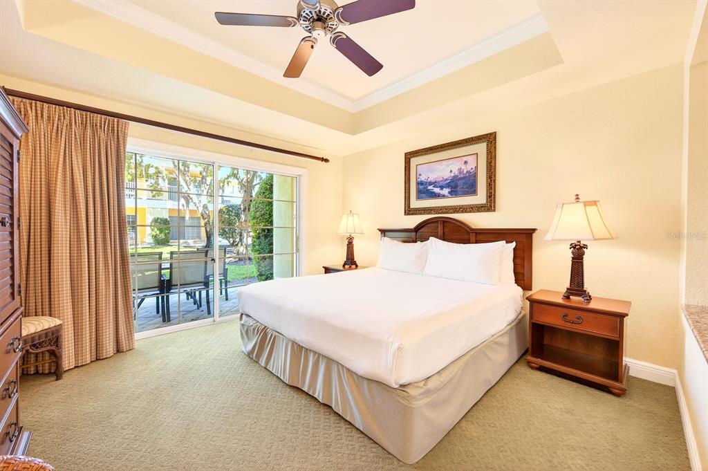 A bedroom features a king bed, ceiling fan, carpeted flooring, and sliding glass doors to a patio — 1302 SEVEN EAGLES COURT UNIT 1302, REUNION, FL