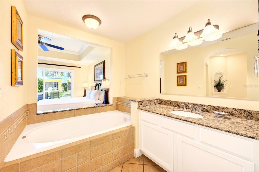 A bathroom features a tiled soaking tub, a granite vanity, and a view into a bedroom — 1302 SEVEN EAGLES COURT UNIT 1302, REUNION, FL