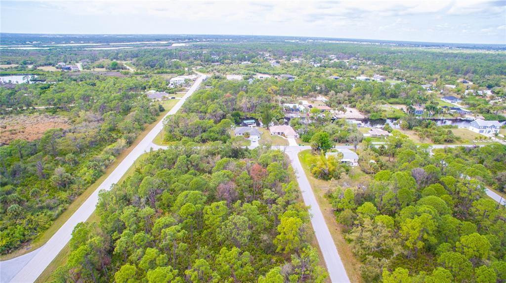 An aerial view shows a residential neighborhood with paved roads, scattered houses, and dense vegetation — 12253 ENDICOTT LANE, PORT CHARLOTTE, FL