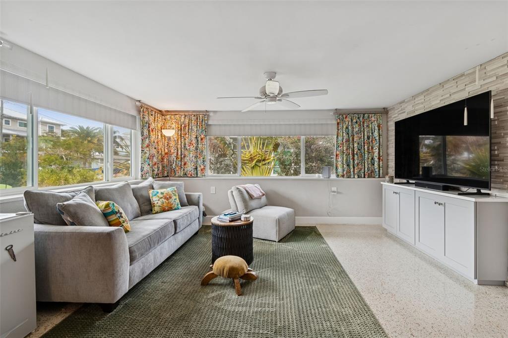 A living room features a grey sofa, a green rug, and a large wall-mounted television — 2427 BAYWOOD DRIVE W, DUNEDIN, FL