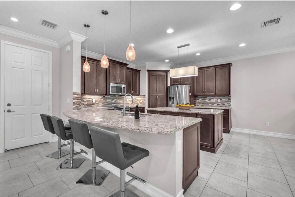 A kitchen features dark wood cabinets, granite countertops, a large island, and gray tile flooring — 8104 Rainforest Jasper Lane, Delray Beach FL 33446, DELRAY BEACH, FL