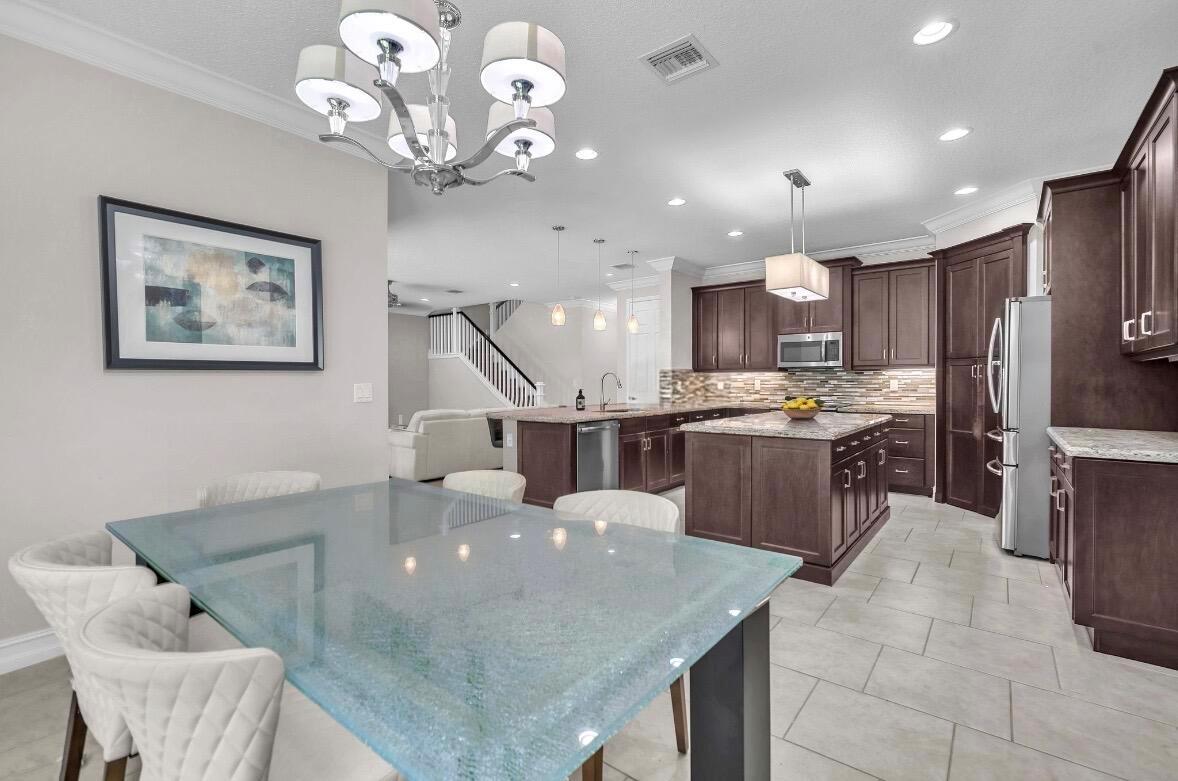 A dining area with a glass table opens into a kitchen featuring dark wood cabinets — 8104 Rainforest Jasper Lane, Delray Beach FL 33446, DELRAY BEACH, FL