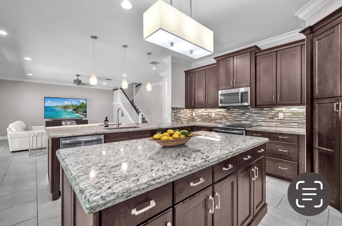 A kitchen with dark wood cabinets, granite countertops, and a large island, overlooking a living area — 8104 Rainforest Jasper Lane, Delray Beach FL 33446, DELRAY BEACH, FL