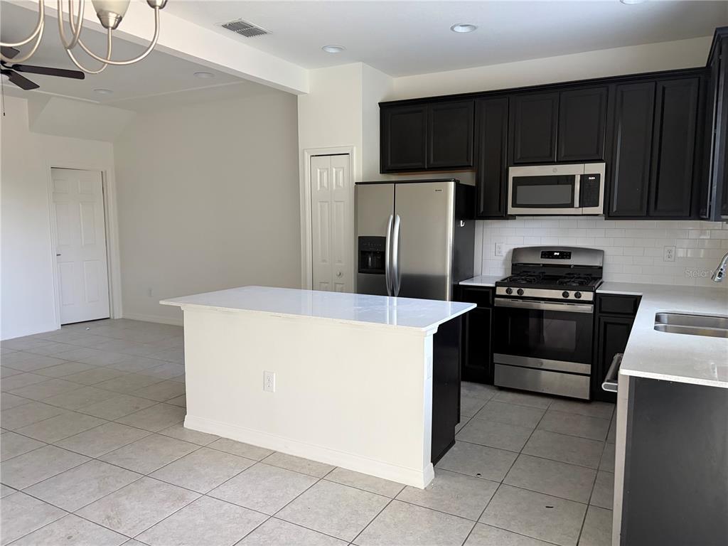 A kitchen features dark cabinets, stainless steel appliances, a white island, and light tile flooring — 6344 CAMINO DRIVE, APOLLO BEACH, FL