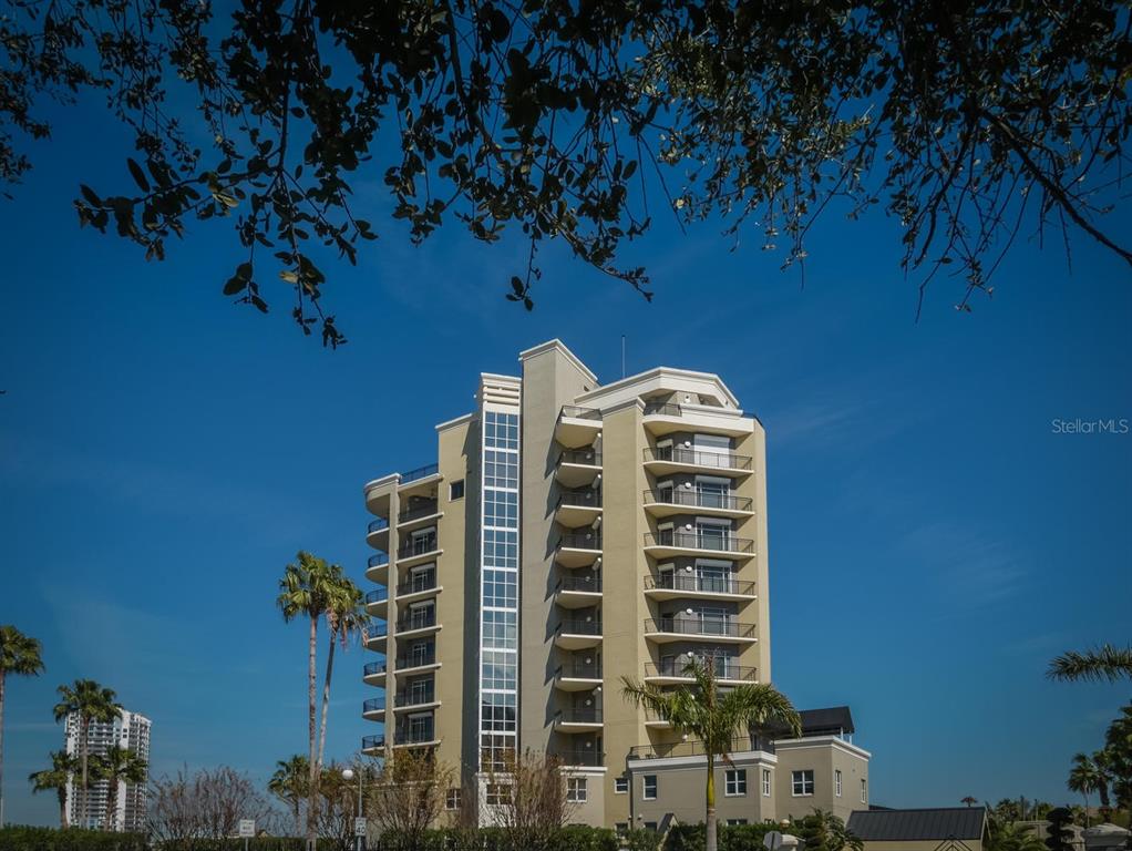 A multi-story beige apartment building stands under a clear blue sky with palm trees — 600 GARRISON COVE LANE UNIT 2B, TAMPA, FL