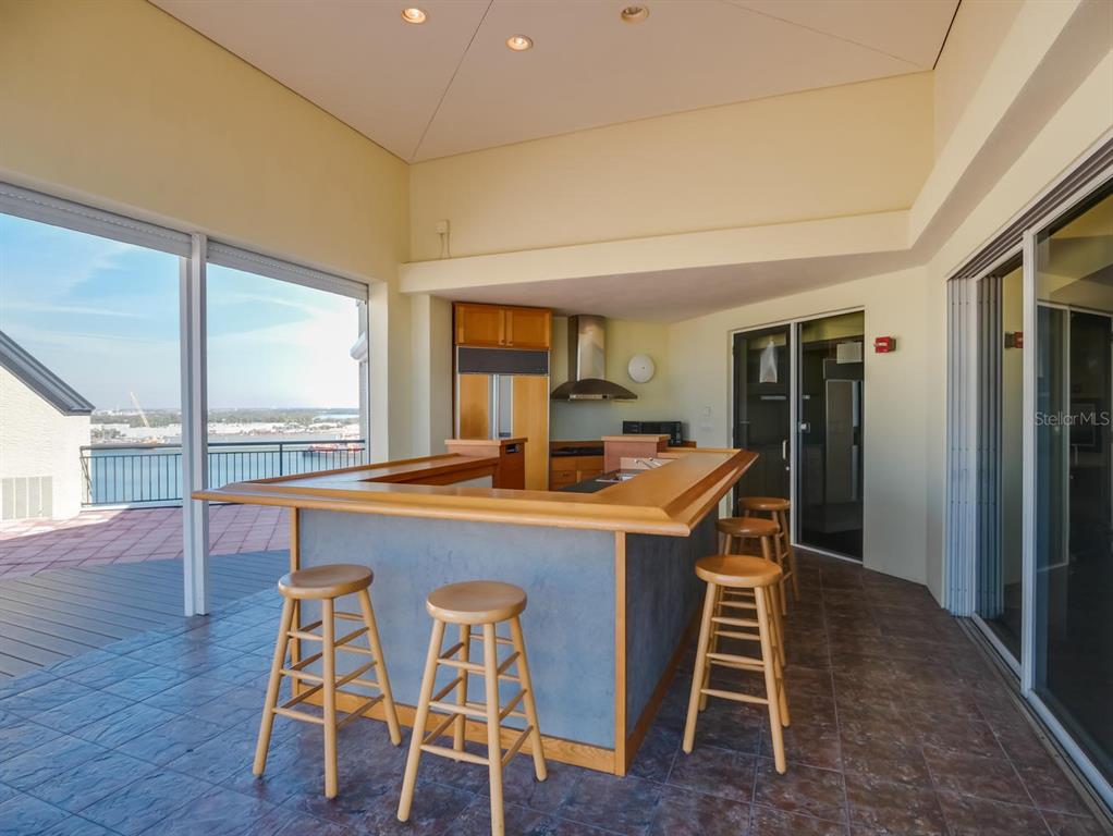 An outdoor kitchen with a bar, wooden stools, and a view of the water — 600 GARRISON COVE LANE UNIT 2B, TAMPA, FL