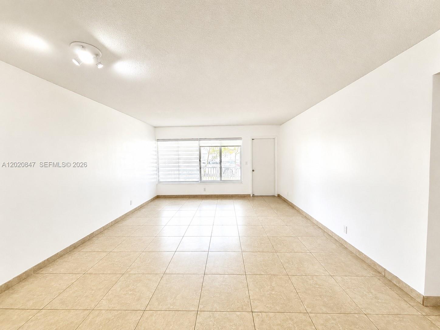An empty room features white walls, beige tile flooring, and a window with blinds — 1460 NE 169th St # 108, North Miami Beach FL 33162, NORTH MIAMI BEACH, FL
