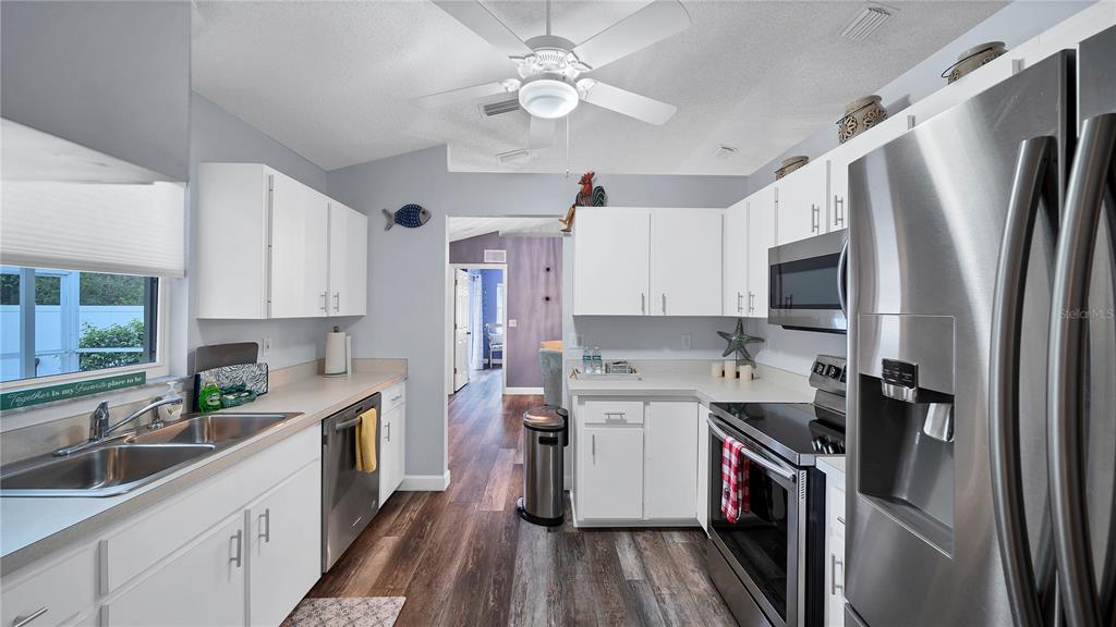 A kitchen features white cabinets, stainless steel appliances, and wood-look flooring — 5219 INVERNESS DRIVE, SARASOTA, FL